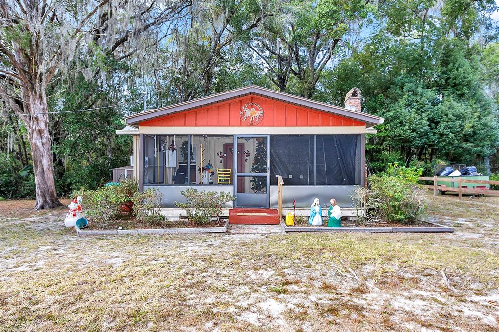 A single-story house with a screened-in porch, red gable trim, and a wooded yard — 20990 W PENNSYLVANIA AVENUE, DUNNELLON, FL