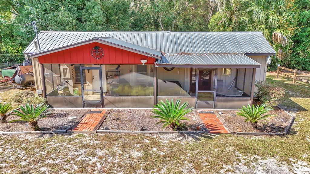 A single-story house with a metal roof and a large screened-in front porch — 20990 W PENNSYLVANIA AVENUE, DUNNELLON, FL