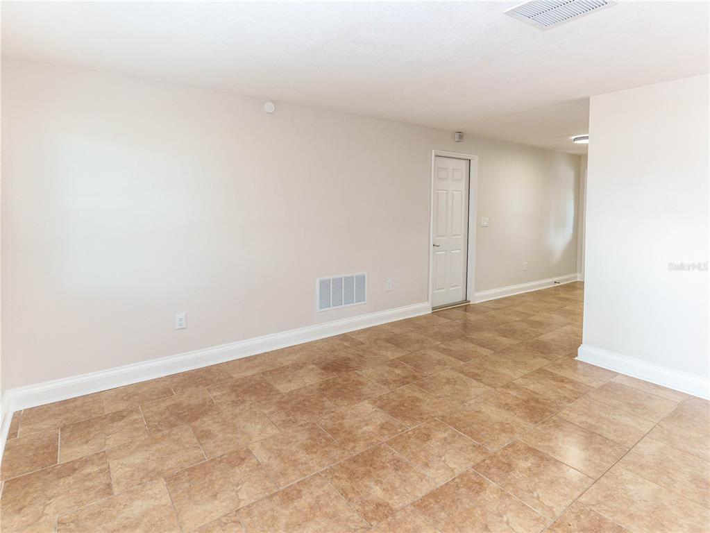 An empty room features beige walls, tan tile flooring, and a white interior door — 7434 MAKO DRIVE, HUDSON, FL
