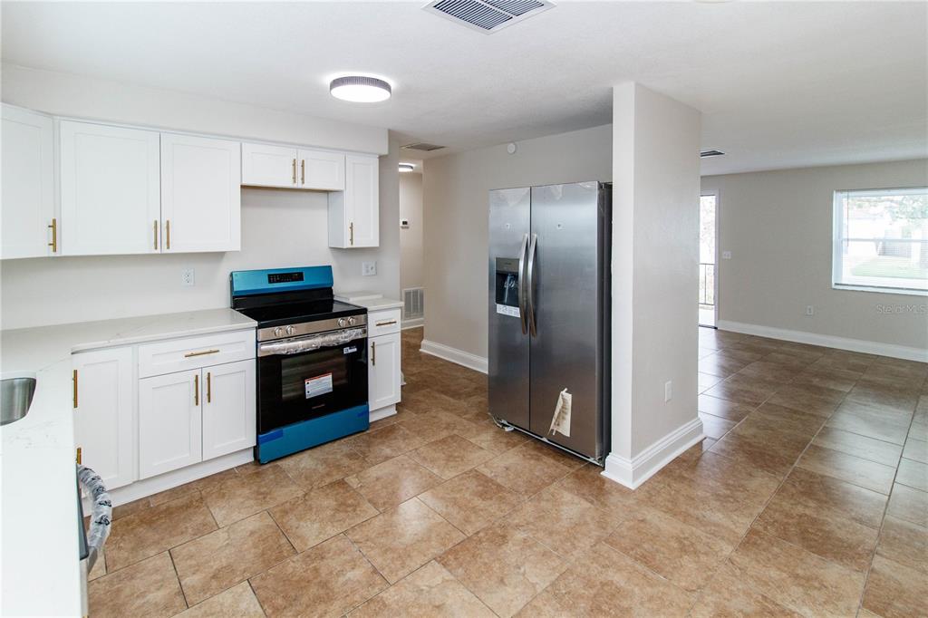 A kitchen with white cabinets, stainless steel appliances, and tan tile flooring — 7434 MAKO DRIVE, HUDSON, FL