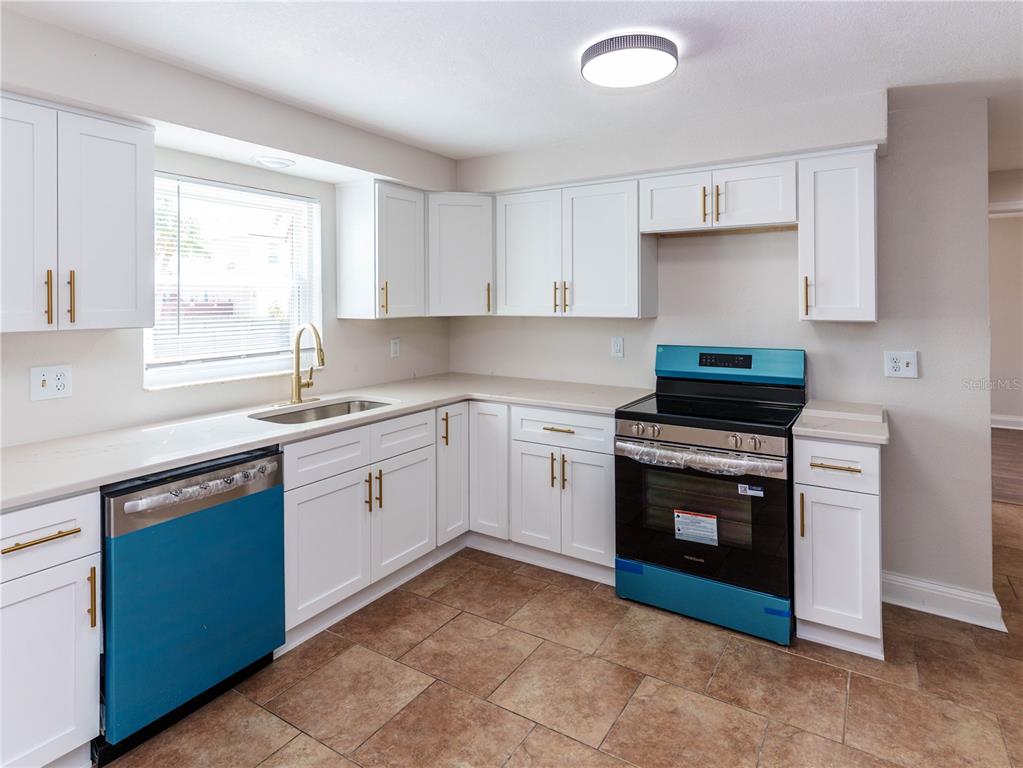 A kitchen features white cabinets, light countertops, stainless steel appliances, and brown tile flooring — 7434 MAKO DRIVE, HUDSON, FL