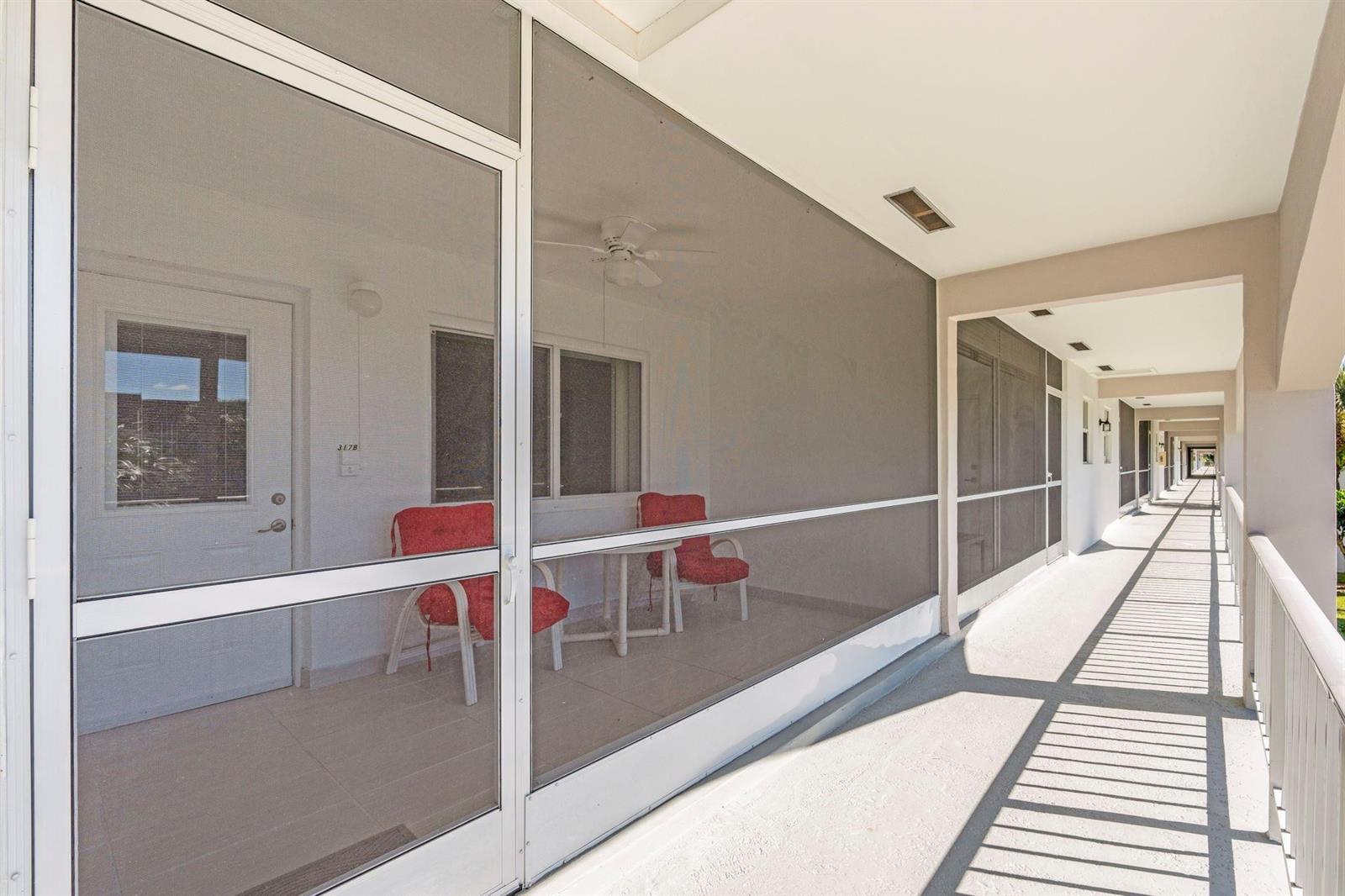 A screened-in balcony with red chairs overlooks an outdoor walkway in a multi-story building — 581 Blue Heron Drive # B, Hallandale Beach FL 33009, HALLANDALE BEACH, FL