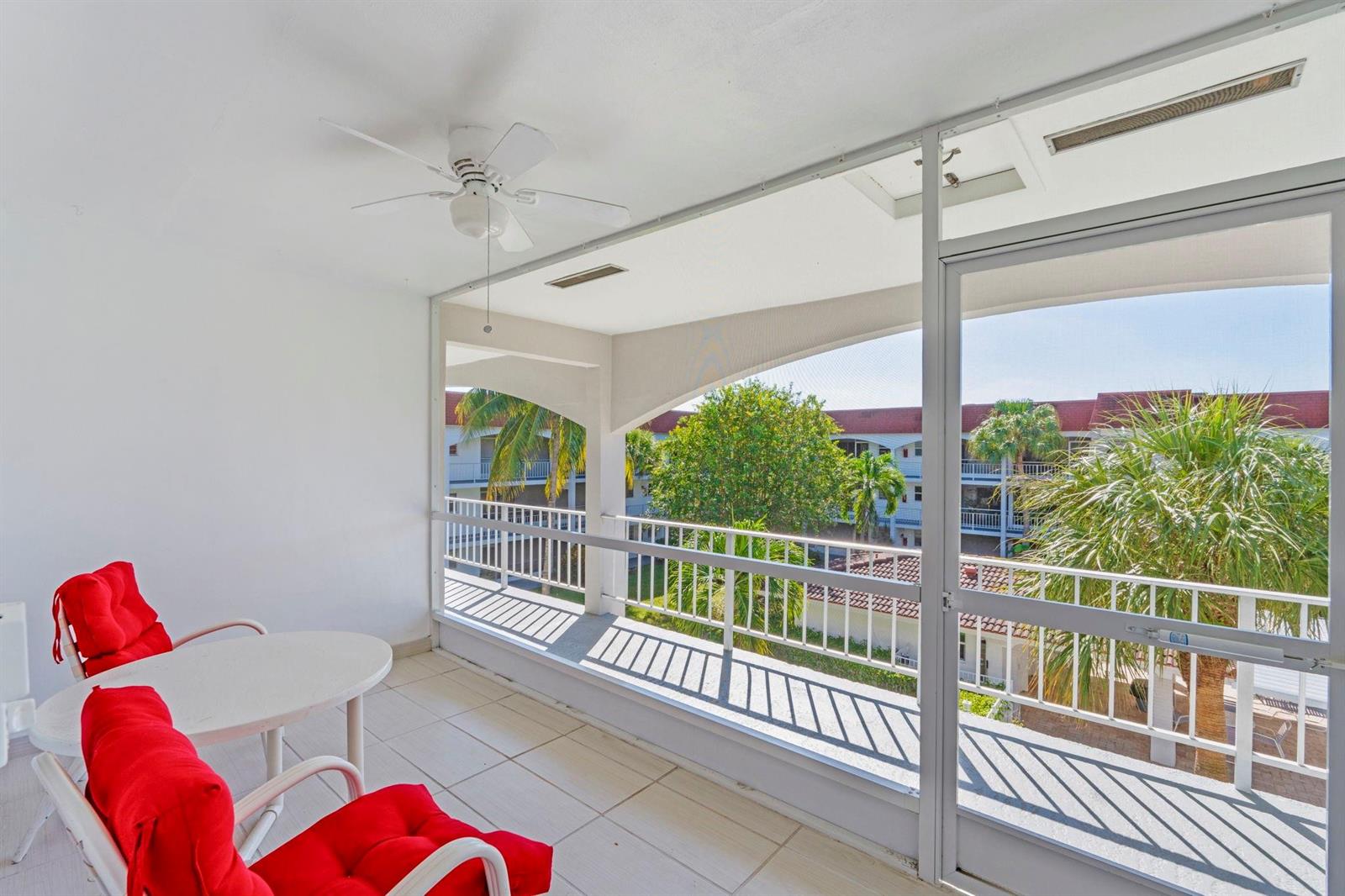 A screened-in balcony features white tile flooring, a ceiling fan, and two red chairs — 581 Blue Heron Drive # B, Hallandale Beach FL 33009, HALLANDALE BEACH, FL