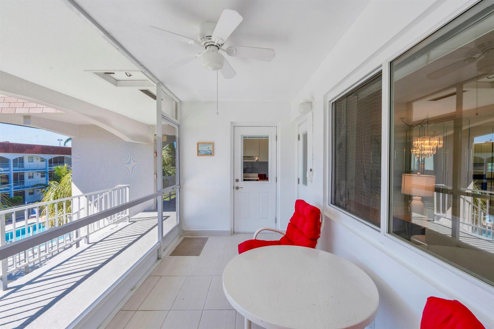 A white-tiled balcony features a ceiling fan, a round table, and a red chair — 581 Blue Heron Drive # B, Hallandale Beach FL 33009, HALLANDALE BEACH, FL
