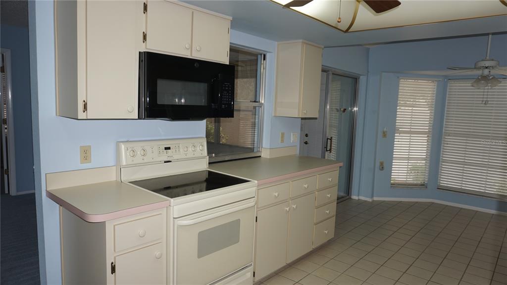 A kitchen with light-colored cabinets, a black microwave, a white stove, and tile flooring — 10512 TAPESTRY DRIVE, PORT RICHEY, FL