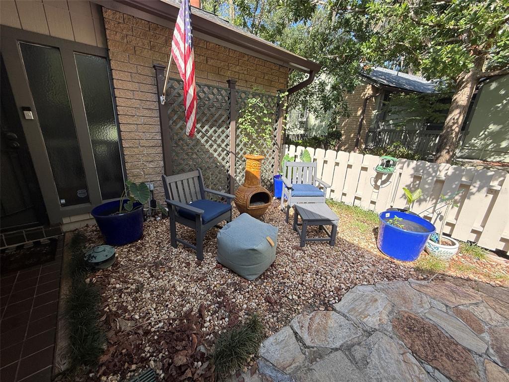 A covered patio features a tiled floor, two chairs with yellow pillows, and a small table — 1629 NW 19TH CIRCLE, GAINESVILLE, FL