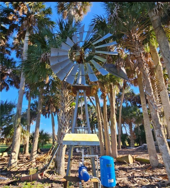 A metal windmill stands in a wooded area with a blue water pump and tank — 320 GRIGSBY ROAD, VENUS, FL