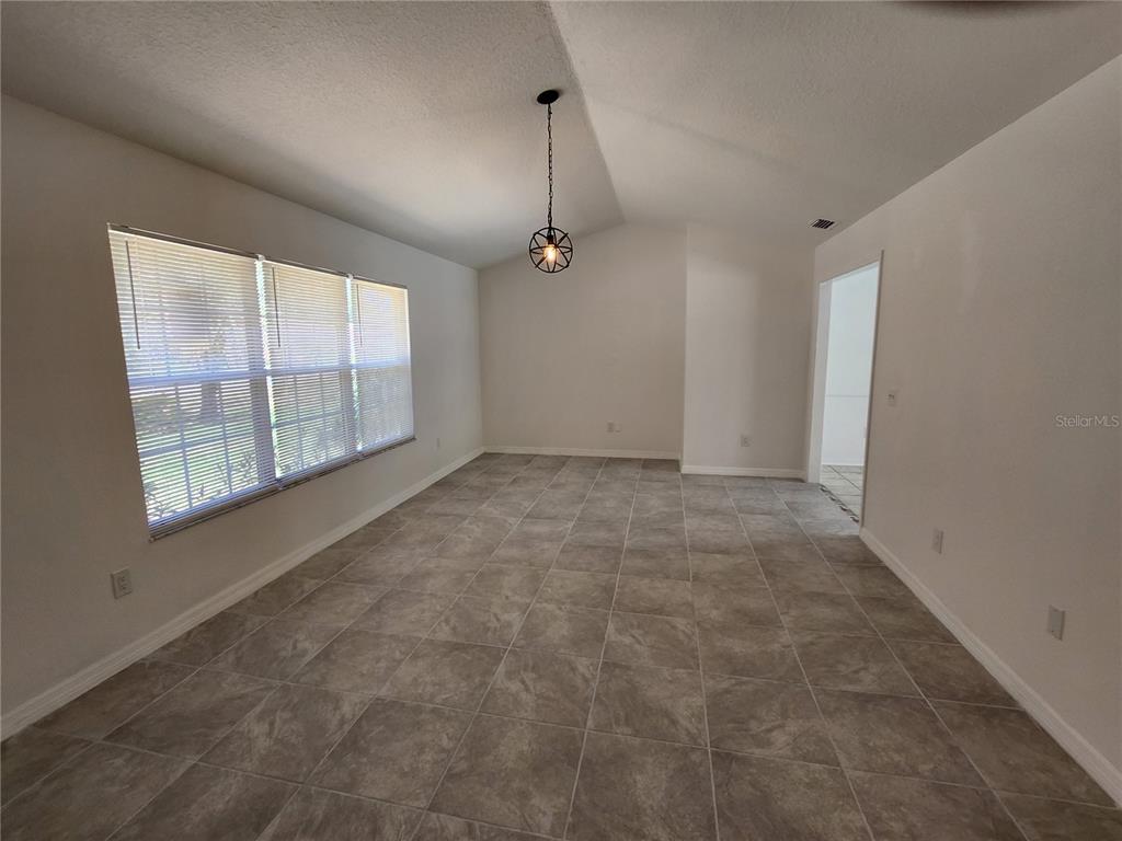 A bright, empty dining room features large windows, a pendant light, and gray tile flooring — 9 TEAK WAY DRIVE, OCALA, FL
