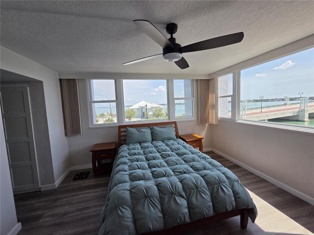 A bedroom with a bed, ceiling fan, and large windows overlooking a bridge and water — 500 TREASURE ISLAND CAUSEWAY UNIT 307, TREASURE ISLAND, FL