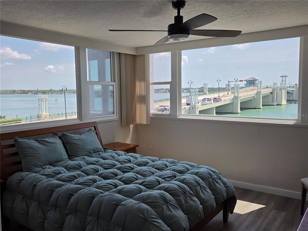 A bedroom with a bed, ceiling fan, and large windows overlooking a bridge and water — 500 TREASURE ISLAND CAUSEWAY UNIT 307, TREASURE ISLAND, FL