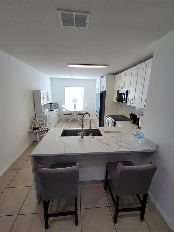 A kitchen features a white quartz waterfall island, gray bar stools, and white cabinetry — 273 ARBOR LAKES DRIVE, DAVENPORT, FL