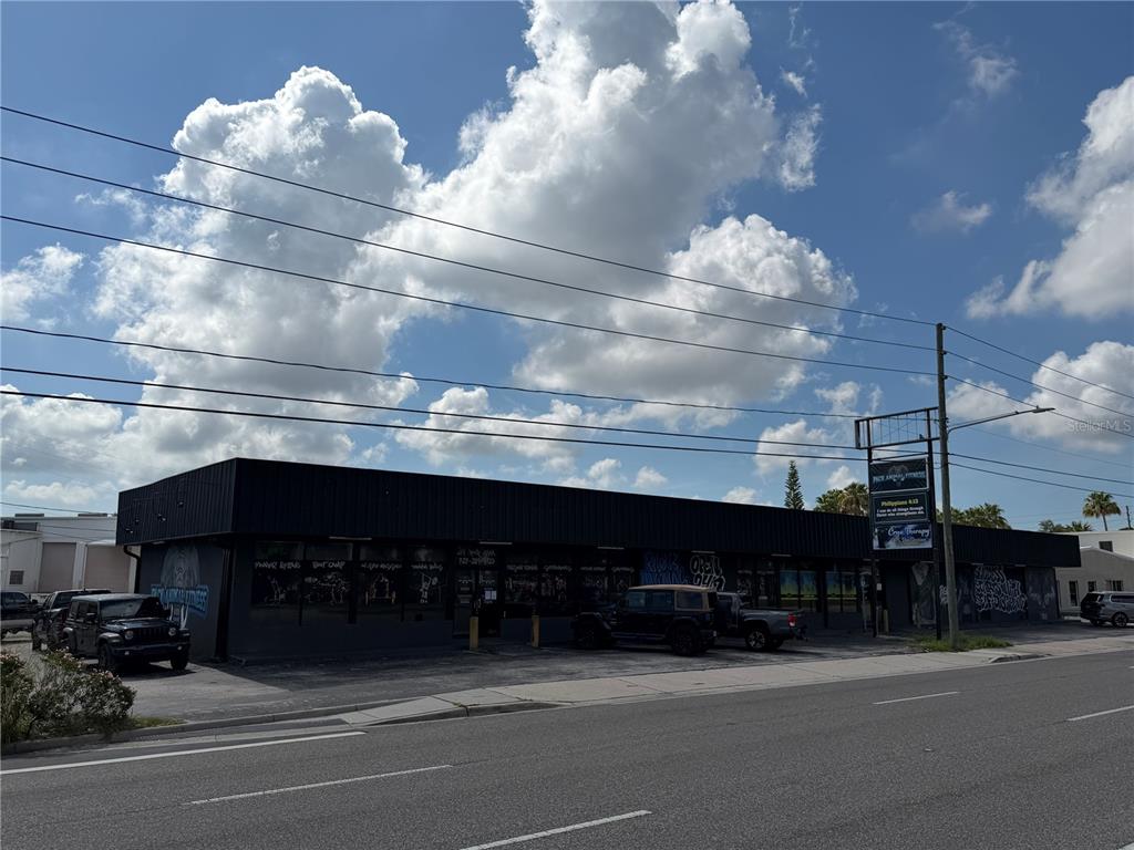 A low-slung commercial building with a black facade and parking lot under a cloudy sky — 5983 49TH STREET N, ST PETERSBURG, FL