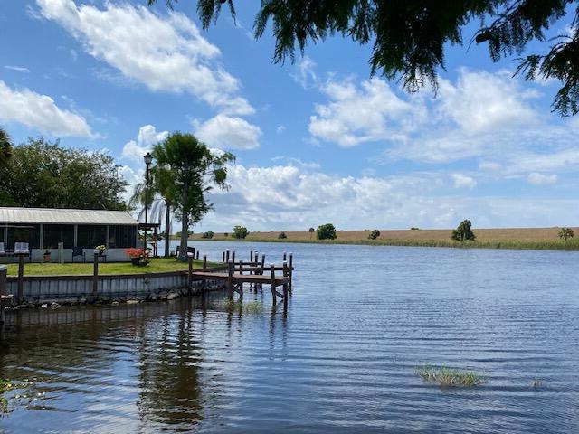 A waterfront house with a wooden dock sits beside a calm river under a blue sky — 8680 Us Highway 441 # B3, Okeechobee FL 34974, OKEECHOBEE, FL