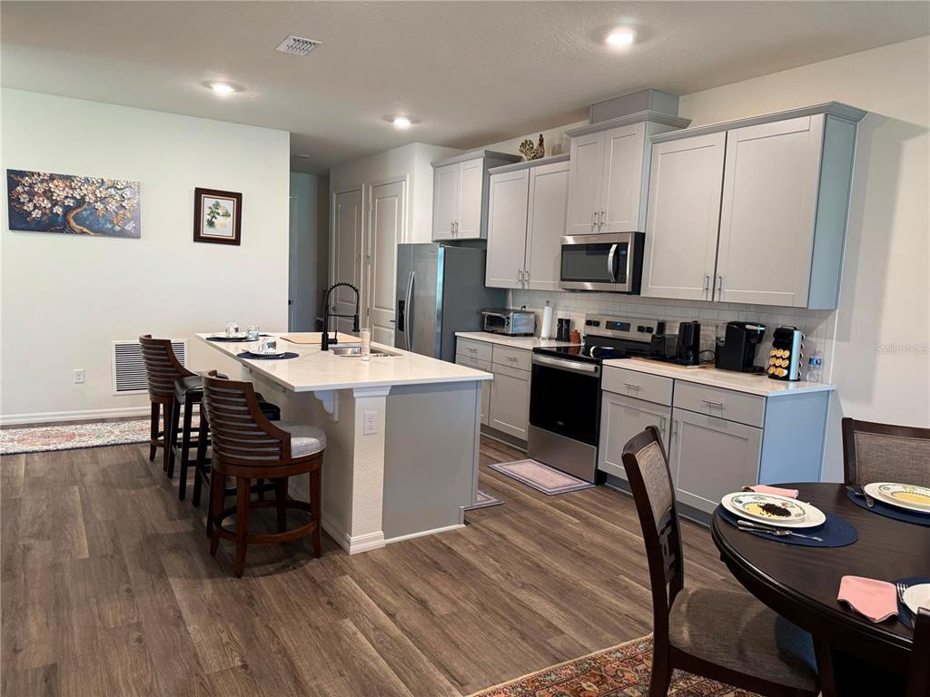 A kitchen features light gray cabinets, a white island with bar seating, and wood-look flooring — 2615 KINSALE LANE, ORMOND BEACH, FL