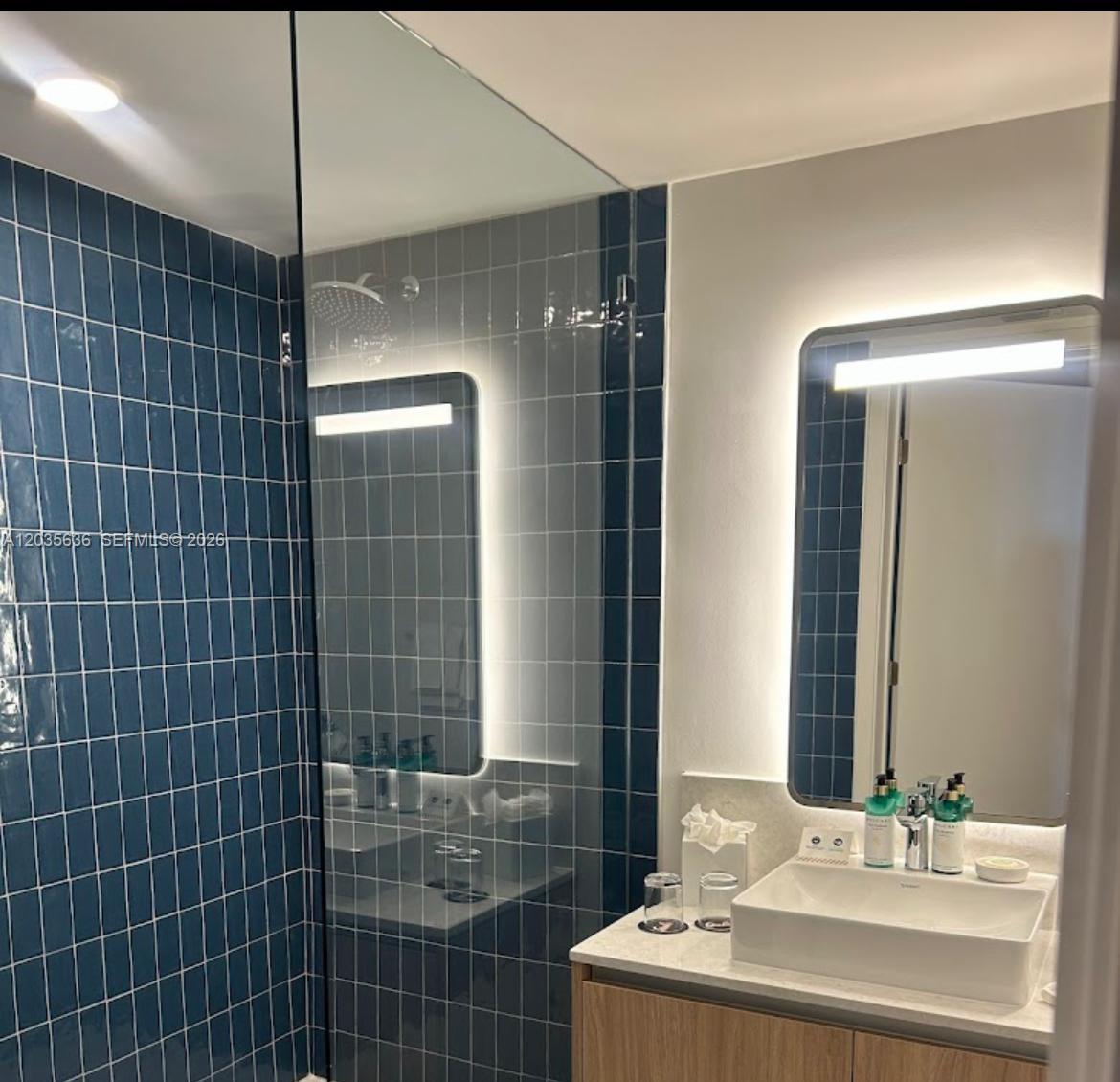 A modern bathroom features a blue tiled shower, a vessel sink, and an illuminated mirror — 601 NE 1st Ave # 1720, Miami FL 33132, MIAMI, FL