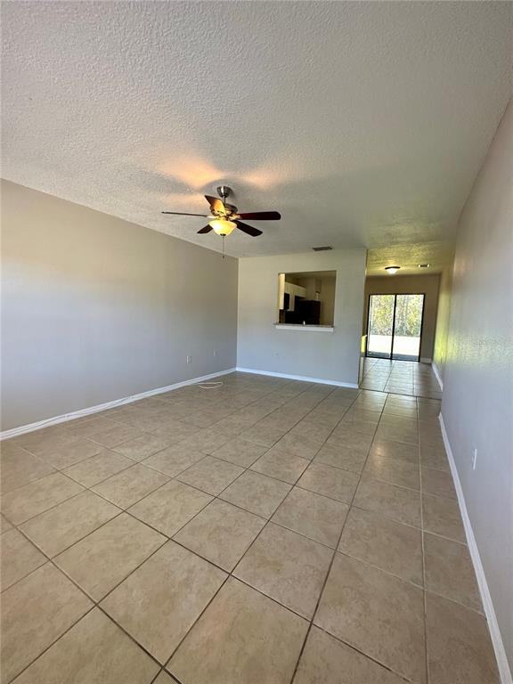 An open-concept living area features beige tile flooring, a ceiling fan, and a kitchen pass-through — 544 IMPERIAL PLACE, KISSIMMEE, FL