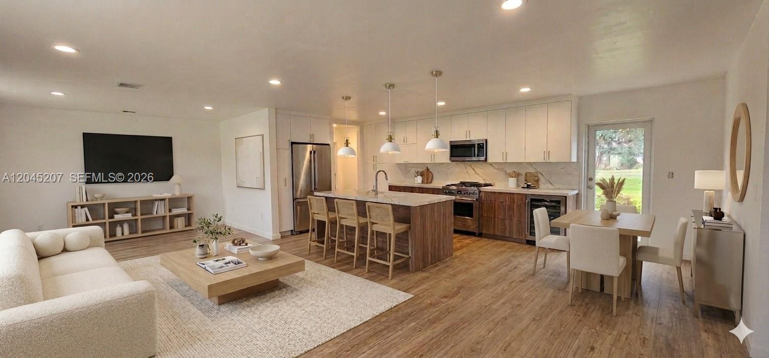 An open-concept living room and kitchen featuring wood flooring, white cabinetry, and a center island — 1233 SW AVENUE C PL, Belle Glade FL 33430, BELLE GLADE, FL