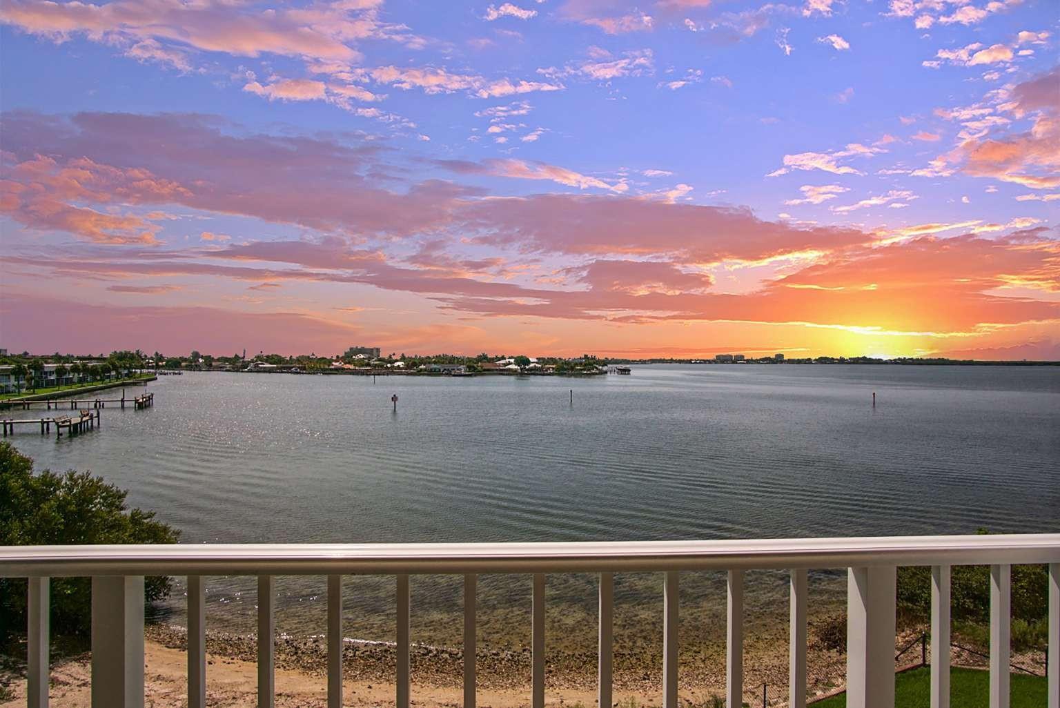A balcony view overlooking a calm bay at sunset with a white railing in foreground — 3 Harbour Isle Drive # 302, Fort Pierce FL 34949, FORT PIERCE, FL