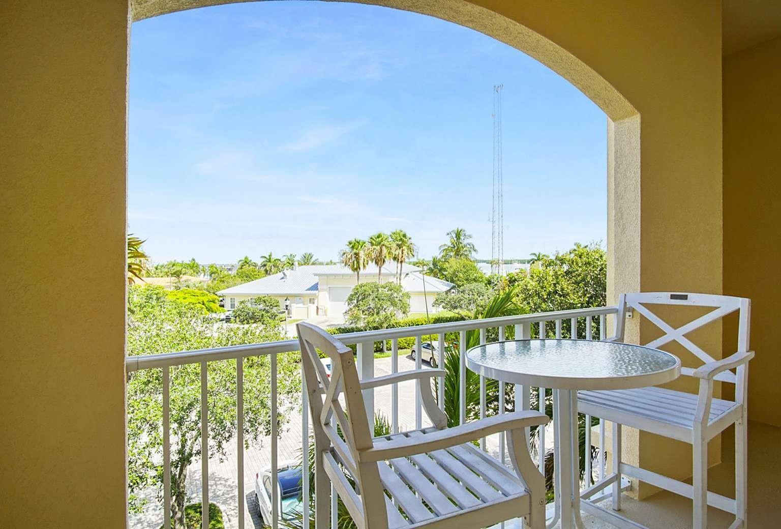 A balcony with a small table and two chairs overlooks a parking area and trees — 3 Harbour Isle Drive # 302, Fort Pierce FL 34949, FORT PIERCE, FL