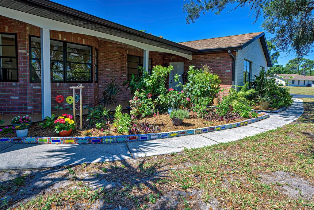A brick house exterior features a covered porch, a garden bed, and a paved walkway — 1061 OWL DRIVE, ENGLEWOOD, FL