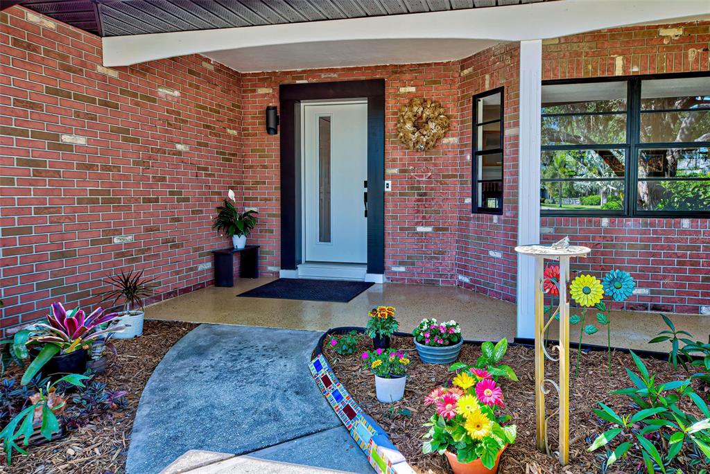 A brick house exterior features a modern white front door, a porch, and garden beds — 1061 OWL DRIVE, ENGLEWOOD, FL