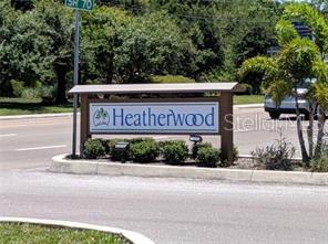 A sign for the Heatherwood community stands near a road with trees and a car — 5323 11TH ST CIRCLE E, BRADENTON, FL