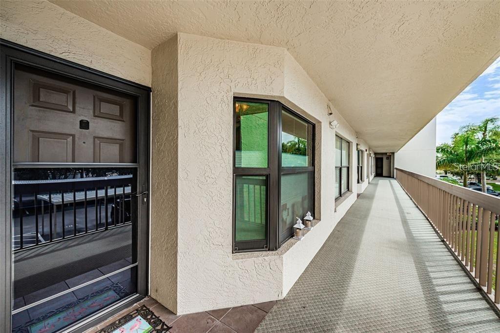 A brown front door and bay window line a long, covered outdoor apartment balcony — 1324 PASADENA AVENUE S UNIT 205, SOUTH PASADENA, FL