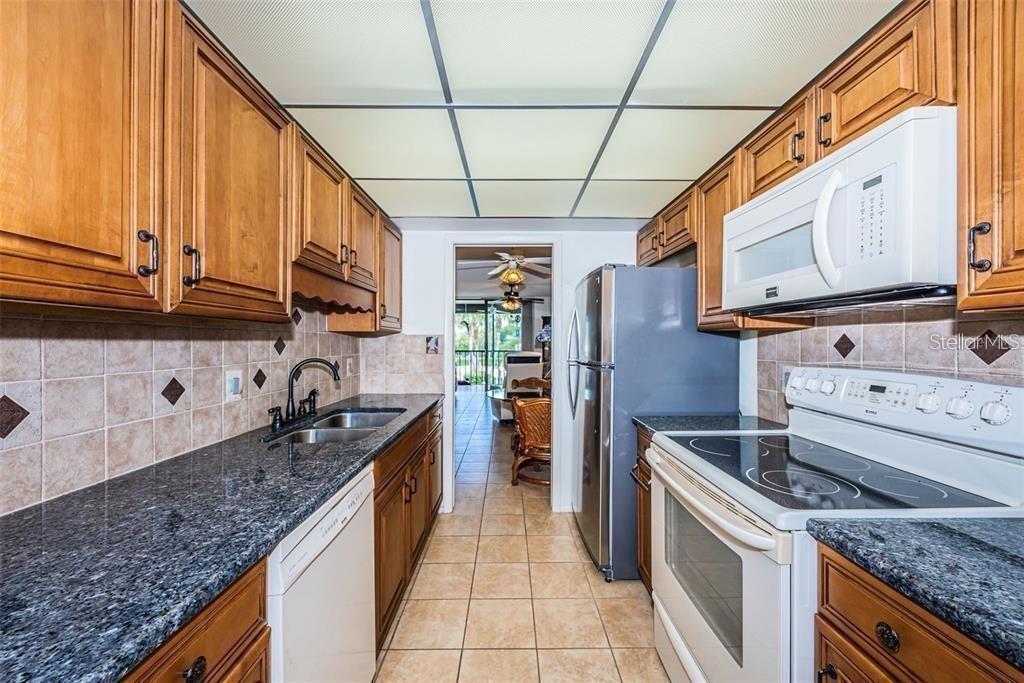 A galley kitchen features wood cabinets, dark granite countertops, and white appliances — 1324 PASADENA AVENUE S UNIT 205, SOUTH PASADENA, FL