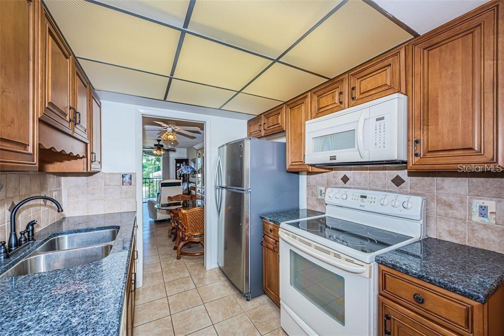 A galley kitchen features wood cabinets, granite countertops, stainless steel appliances, and a drop ceiling — 1324 PASADENA AVENUE S UNIT 205, SOUTH PASADENA, FL