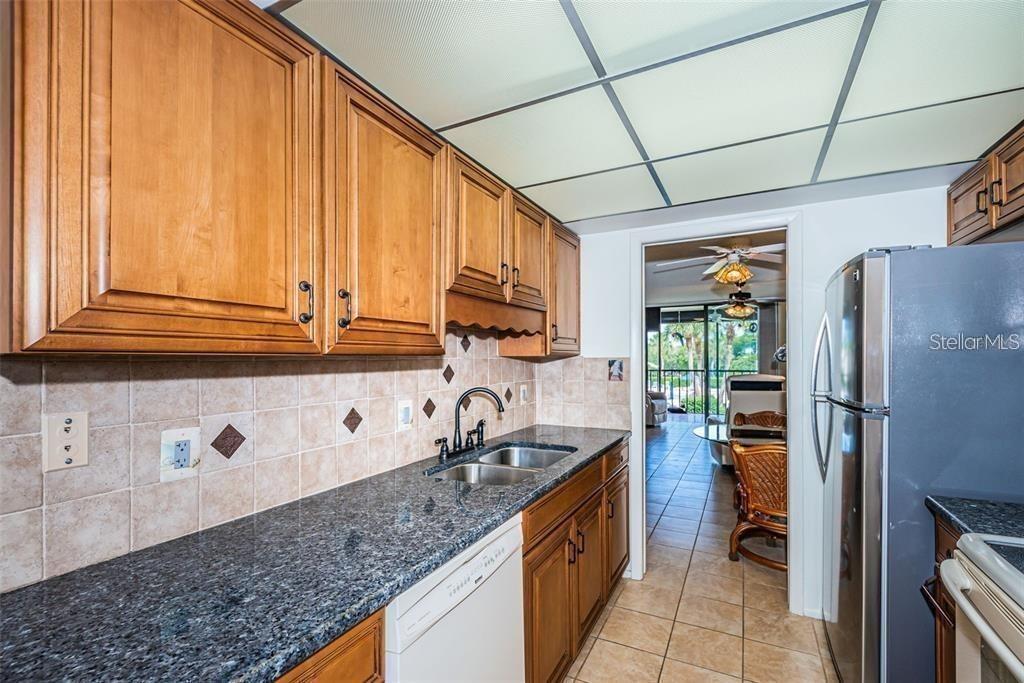 A kitchen features wood cabinets, granite countertops, a double sink, and a stainless steel refrigerator — 1324 PASADENA AVENUE S UNIT 205, SOUTH PASADENA, FL
