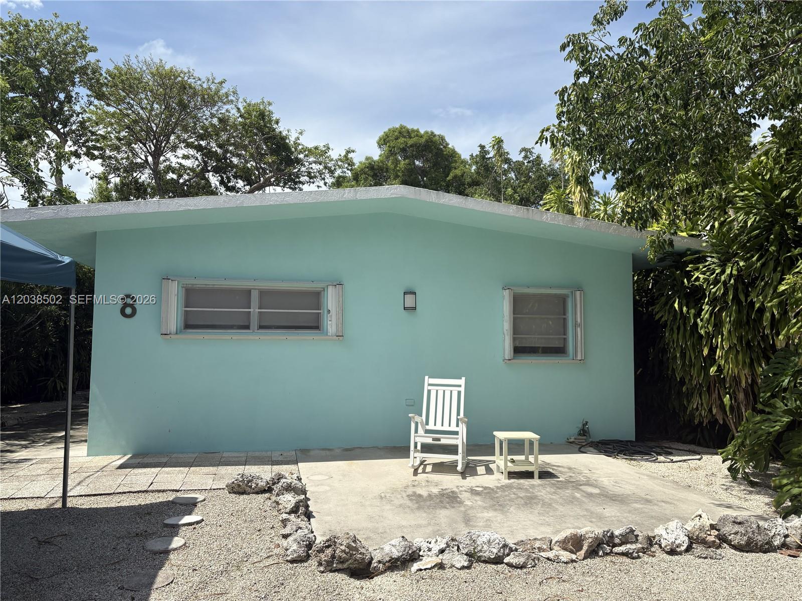 A light blue exterior wall features two windows, a white rocking chair, and a small table — 8 Jewfish Ave, Key Largo FL 33037, KEY LARGO, FL