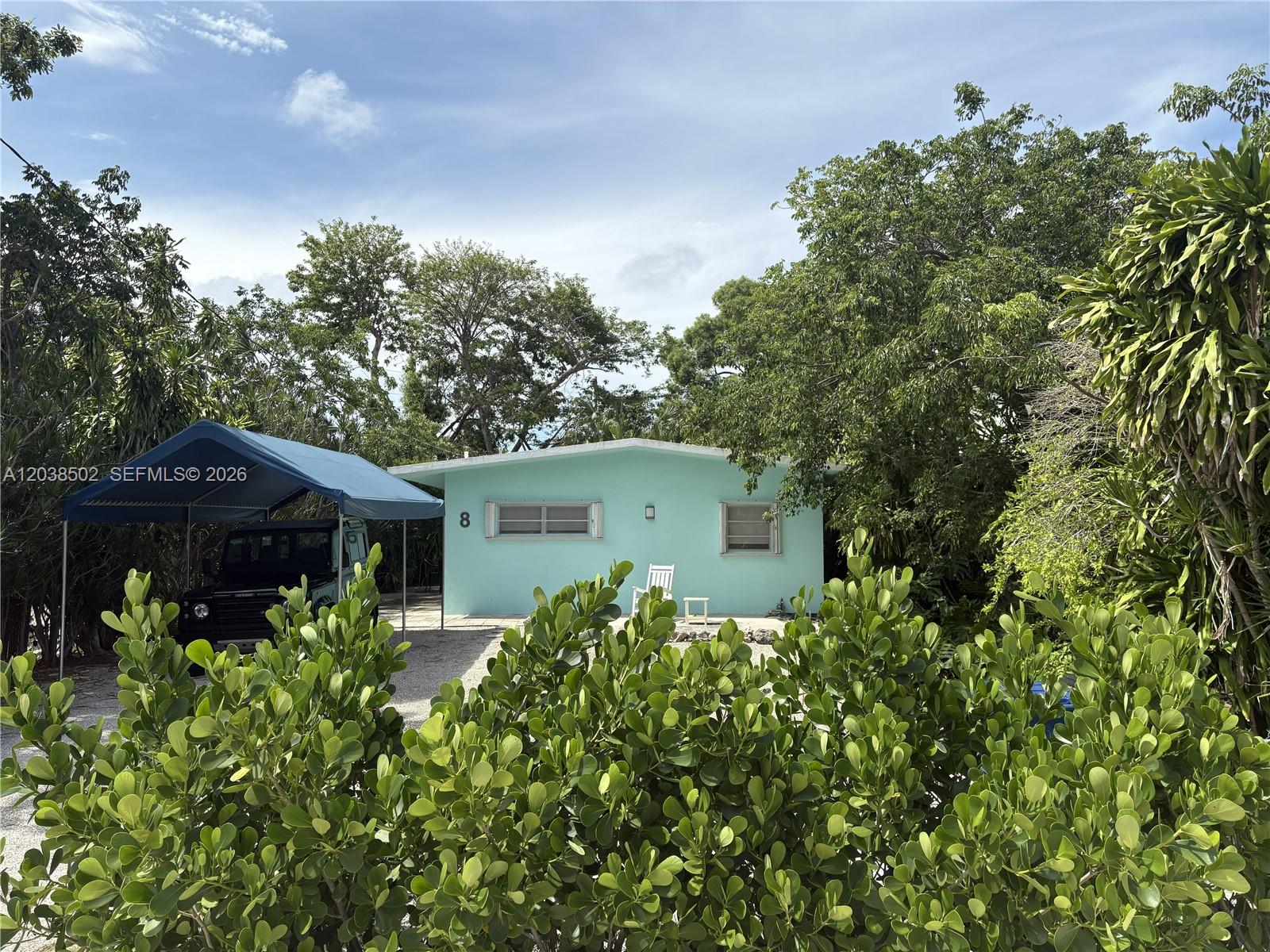 A light blue single-story house features a carport with a vehicle and surrounding lush trees — 8 Jewfish Ave, Key Largo FL 33037, KEY LARGO, FL