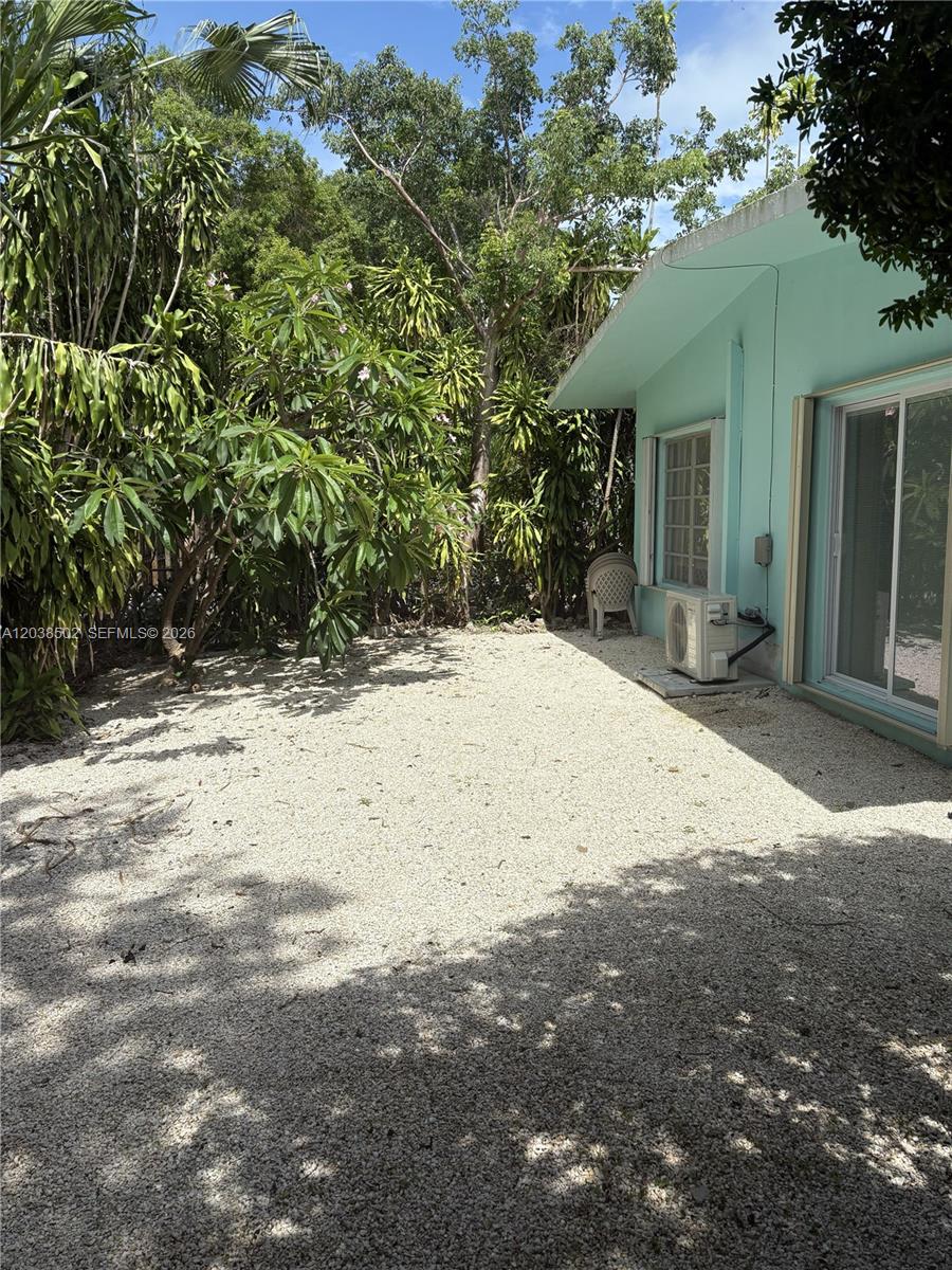 A gravel backyard area sits beside a light blue house with a sliding glass door — 8 Jewfish Ave, Key Largo FL 33037, KEY LARGO, FL