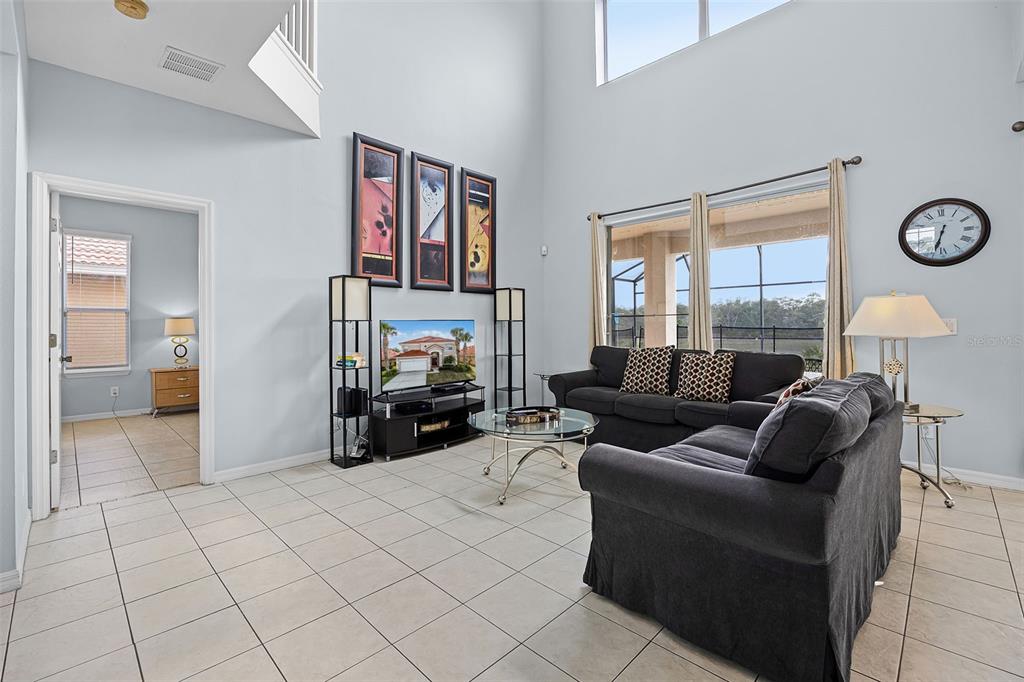 A living room with tile floors, a dark sofa, a glass coffee table, and high ceilings — 321 ROSSO DRIVE, DAVENPORT, FL