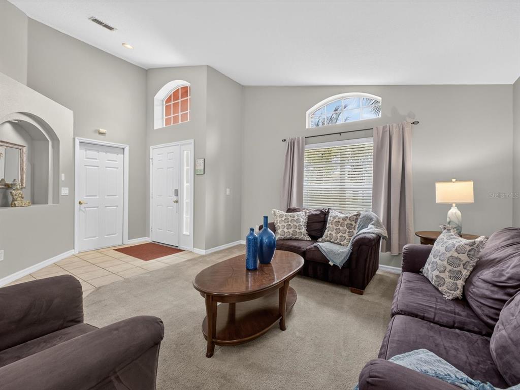 A living room with high ceilings, beige carpet, and dark brown furniture near an entryway — 554 PALOMA DRIVE, DAVENPORT, FL