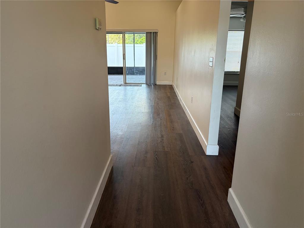 A hallway with dark wood-look flooring leads to a living area with a sliding glass door — 11516 WHISPERING HOLLOW DRIVE, TAMPA, FL
