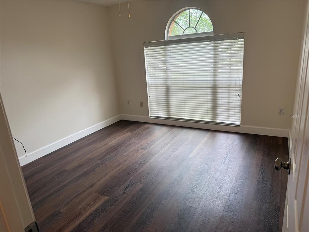 An empty room features dark wood-look flooring, beige walls, and a large arched window — 11516 WHISPERING HOLLOW DRIVE, TAMPA, FL