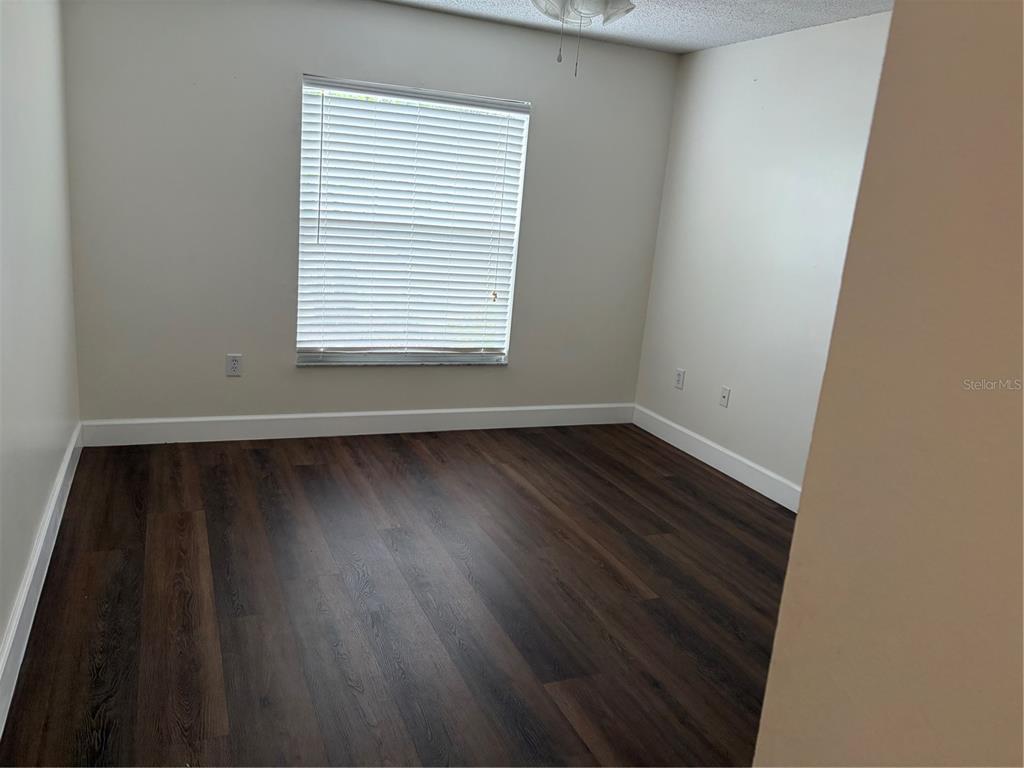 An empty bedroom features dark wood-look flooring, light-colored walls, and a window with white blinds — 11516 WHISPERING HOLLOW DRIVE, TAMPA, FL