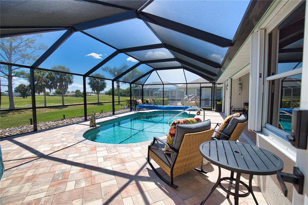 A screened-in patio features a swimming pool, stone pavers, and outdoor furniture overlooking a golf course — 22 MEDALIST COURT, ROTONDA WEST, FL