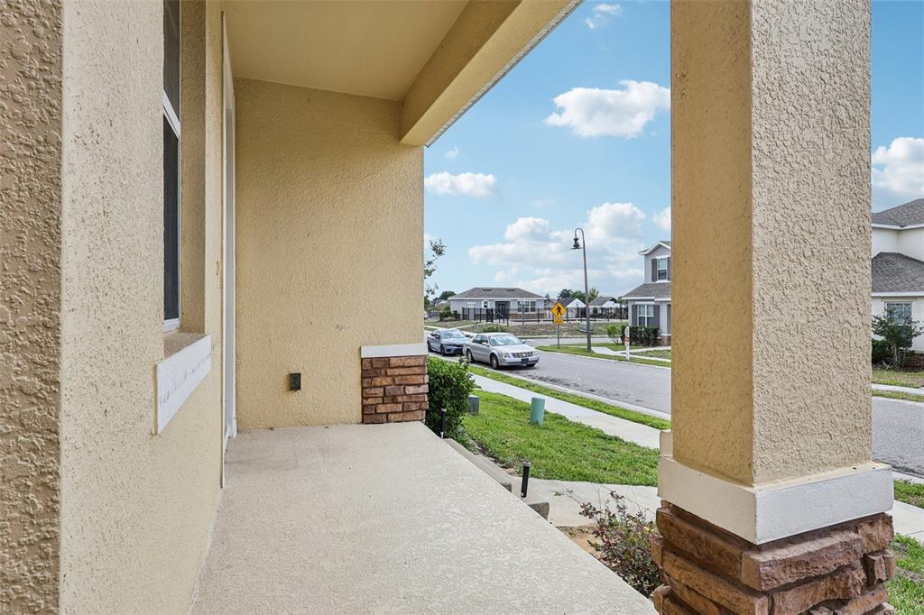A covered front porch with a concrete floor, stucco walls, and stone-accented support columns — 203 BOYDFIELD LANE, DAVENPORT, FL