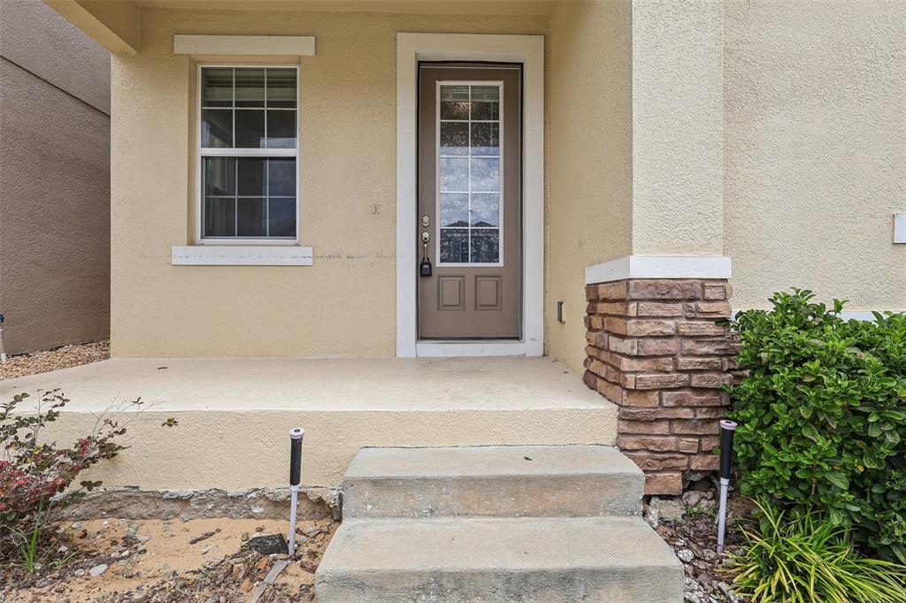 A beige house exterior features a front door with a window, stone accents, and steps — 203 BOYDFIELD LANE, DAVENPORT, FL