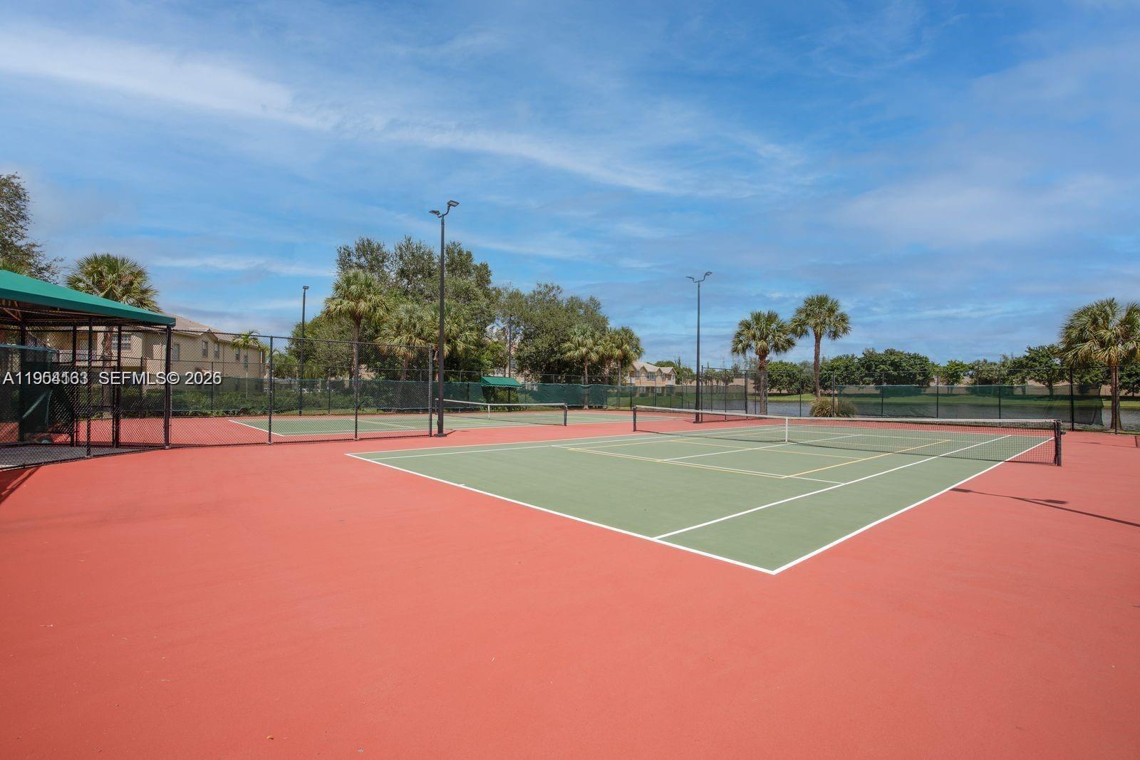 A tennis court with a green surface and red surrounding area sits under a blue sky — 13216 SW 44th St # 11204, Miramar FL 33027, MIRAMAR, FL