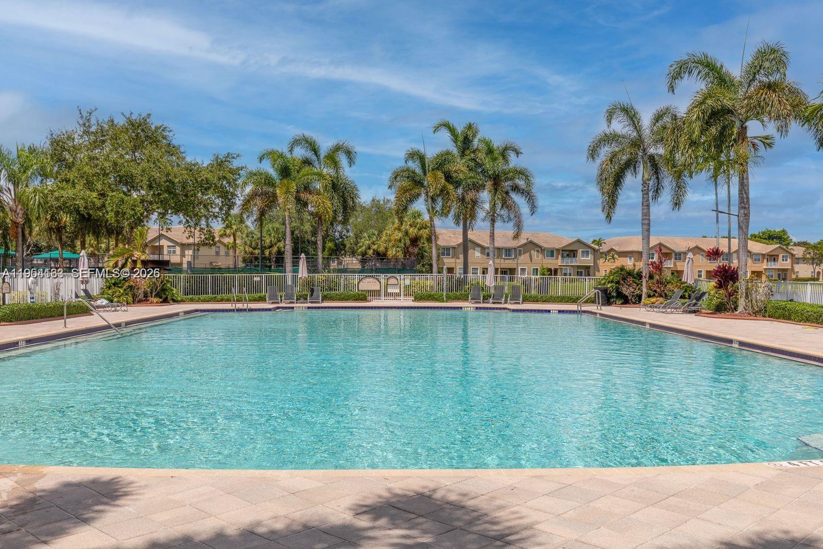 A large rectangular swimming pool is surrounded by a paved deck, palm trees, and buildings — 13216 SW 44th St # 11204, Miramar FL 33027, MIRAMAR, FL