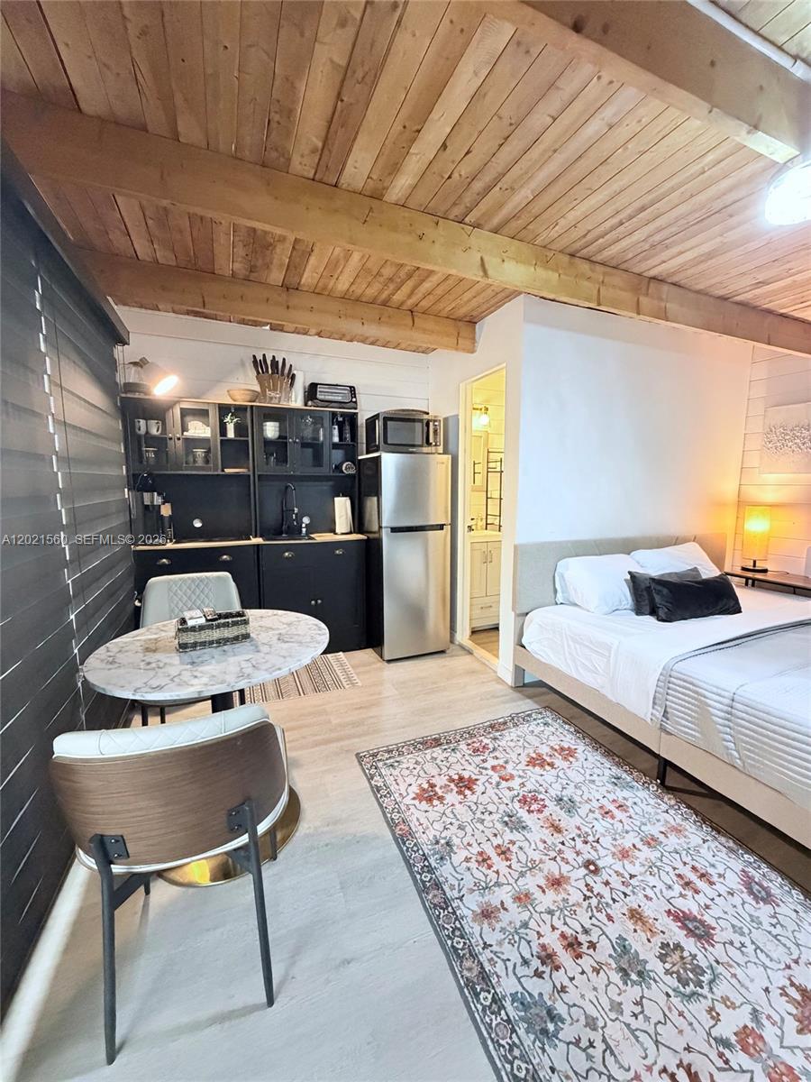 A studio apartment features a kitchenette, a dining table, and a bed under wood-beamed ceilings — TAVERNIER, FL