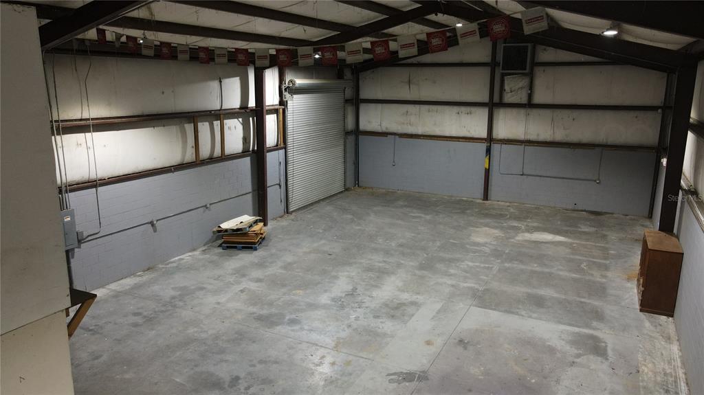 An empty industrial warehouse space features concrete floors, gray block walls, and a roll-up door — 3720 NE 47TH PLACE, OCALA, FL
