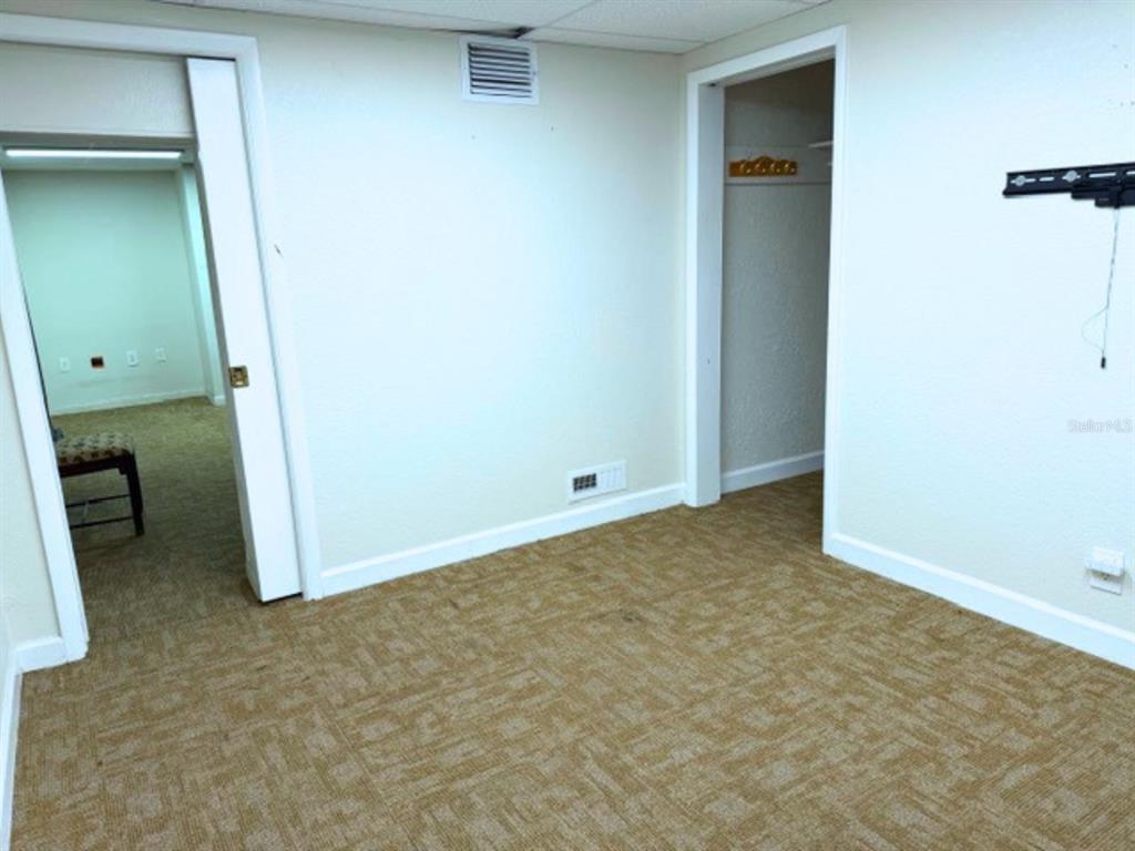 A room with tan carpet, white walls, two doorways, and a wall-mounted television bracket — 208 13TH STREET SW, LARGO, FL