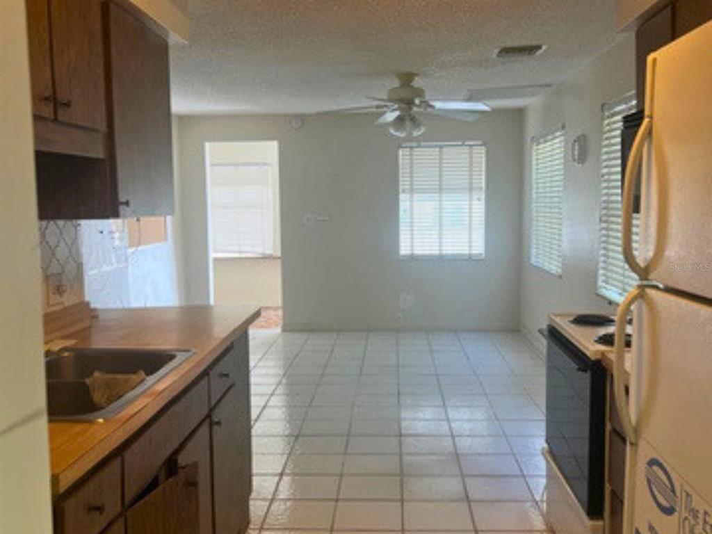 A kitchen with wood cabinets and tile flooring opens into a dining area with windows — 208 13TH STREET SW, LARGO, FL