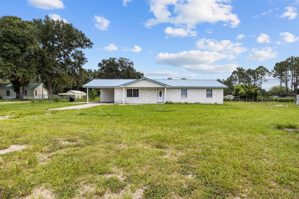 A single-story white stone house with a metal roof and an attached carport — 9545 STATE ROAD 33 N, POLK CITY, FL