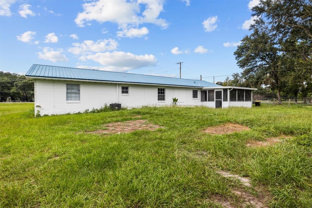 The exterior of a white single-story house with a blue metal roof and screened porch — 9545 STATE ROAD 33 N, POLK CITY, FL
