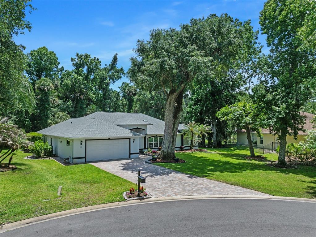 A single-story house with a white exterior, dark trim, and a paved driveway sits among trees — 10 COTTON MILL COURT, ORMOND BEACH, FL